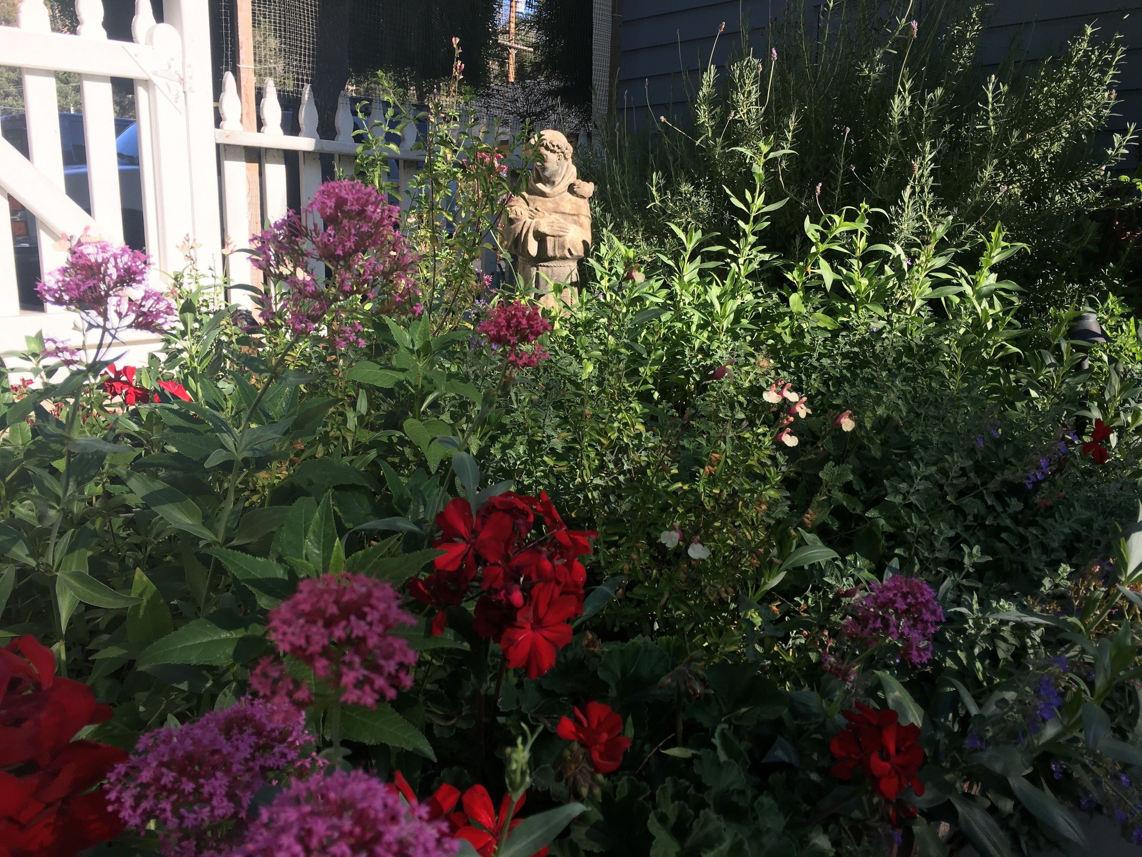 A garden with various flowers and a statue in the background.
