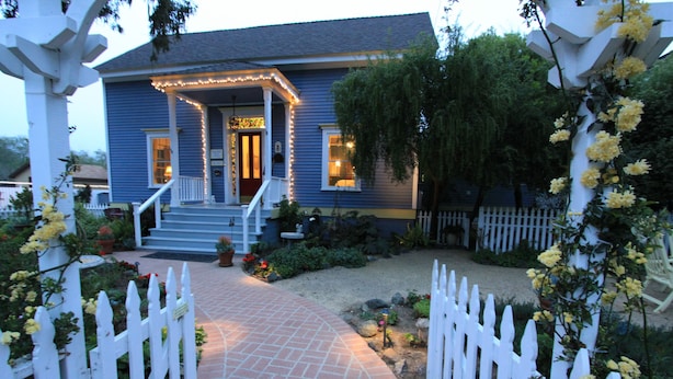 A blue house with a porch, white picket fence, and yellow flowers. - Olallieberry Inn B&B (Cambria)