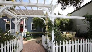 A garden with a white picket fence, a brick pathway, and a pergola structure. - Olallieberry Inn B&B (Cambria)