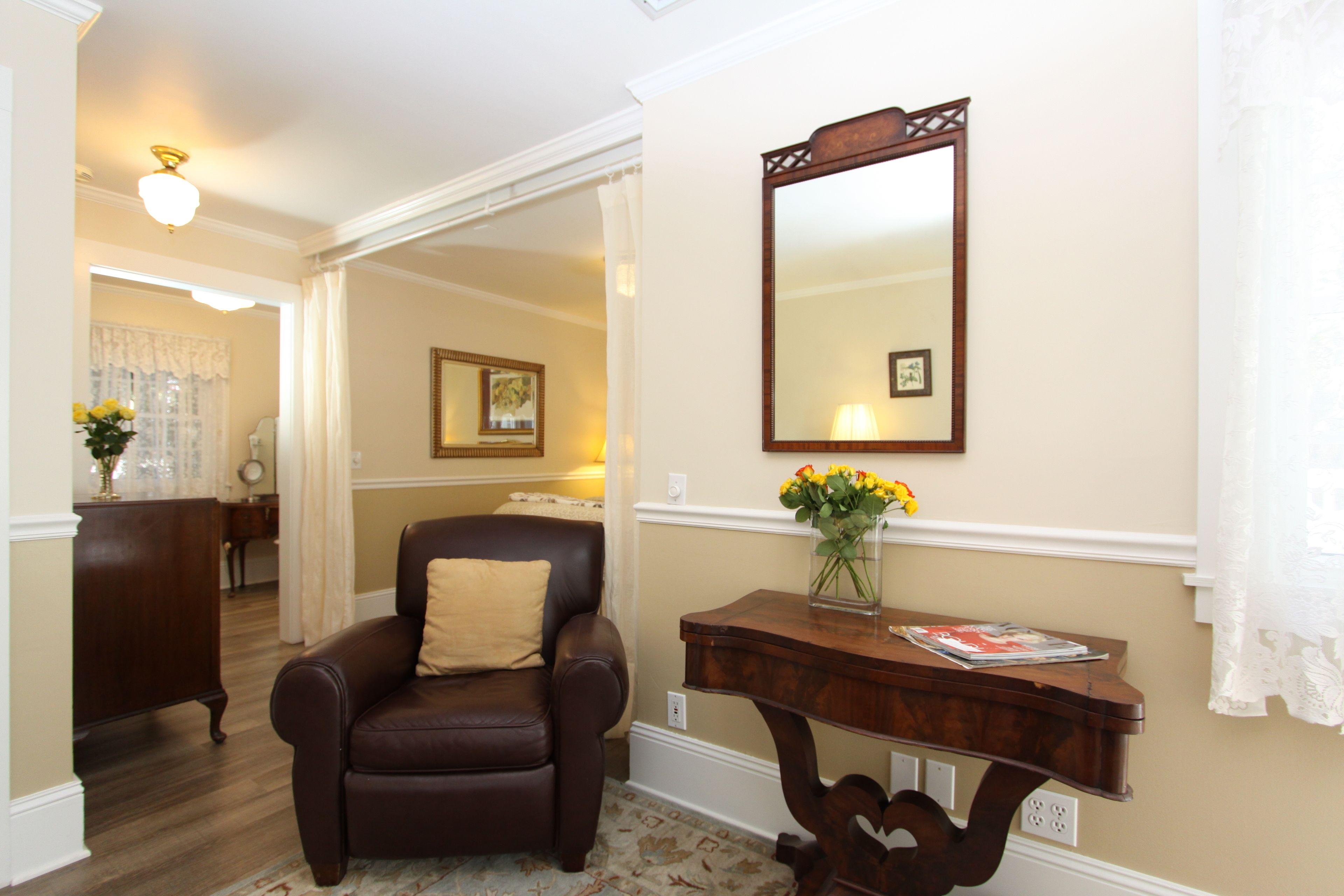 Un salón con un sillón de cuero marrón, una consola de madera con un jarrón de flores y un espejo grande en la pared.