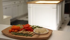 A wooden cutting board with vegetables, crackers, and a bowl of dip on a kitchen counter. - Olallieberry Inn B&B (Cambria)