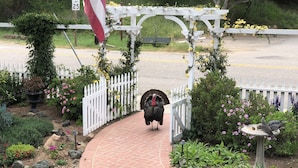 A turkeys walking on a brick pathway surrounded by a garden with a white picket fence, a bird feeder, and a welcome sign. - Olallieberry Inn B&B (Cambria)