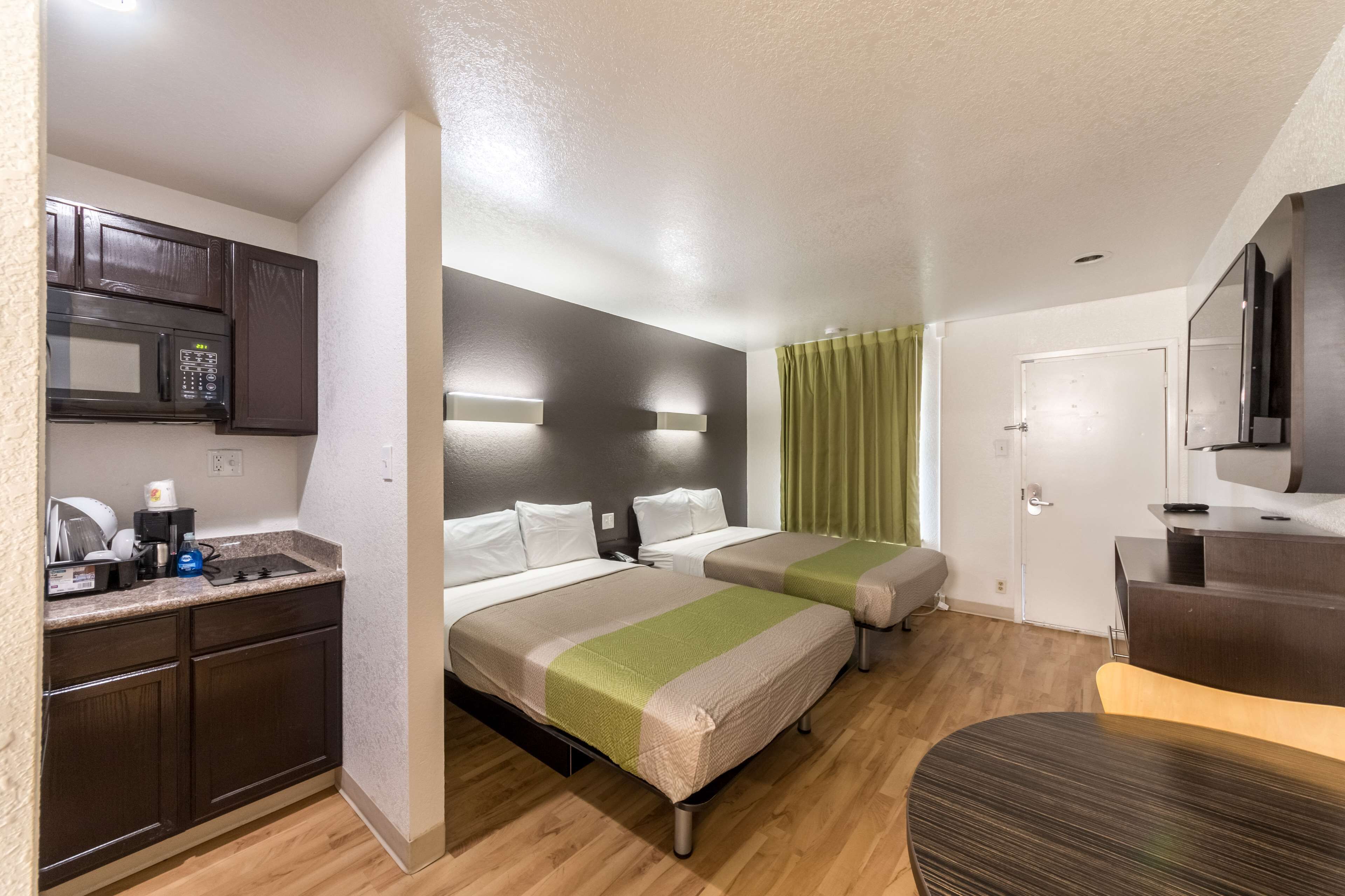 A hotel room with two beds, a kitchenette, a flat-screen TV, and a wooden floor.