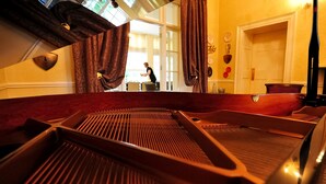 Una habitación con un piano, un ventanal grande y cortinas.