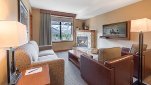 A hotel room with a fireplace, a sofa, a TV, and a window with a mountain view. - Falcon Crest Lodge by CLIQUE (Canmore)