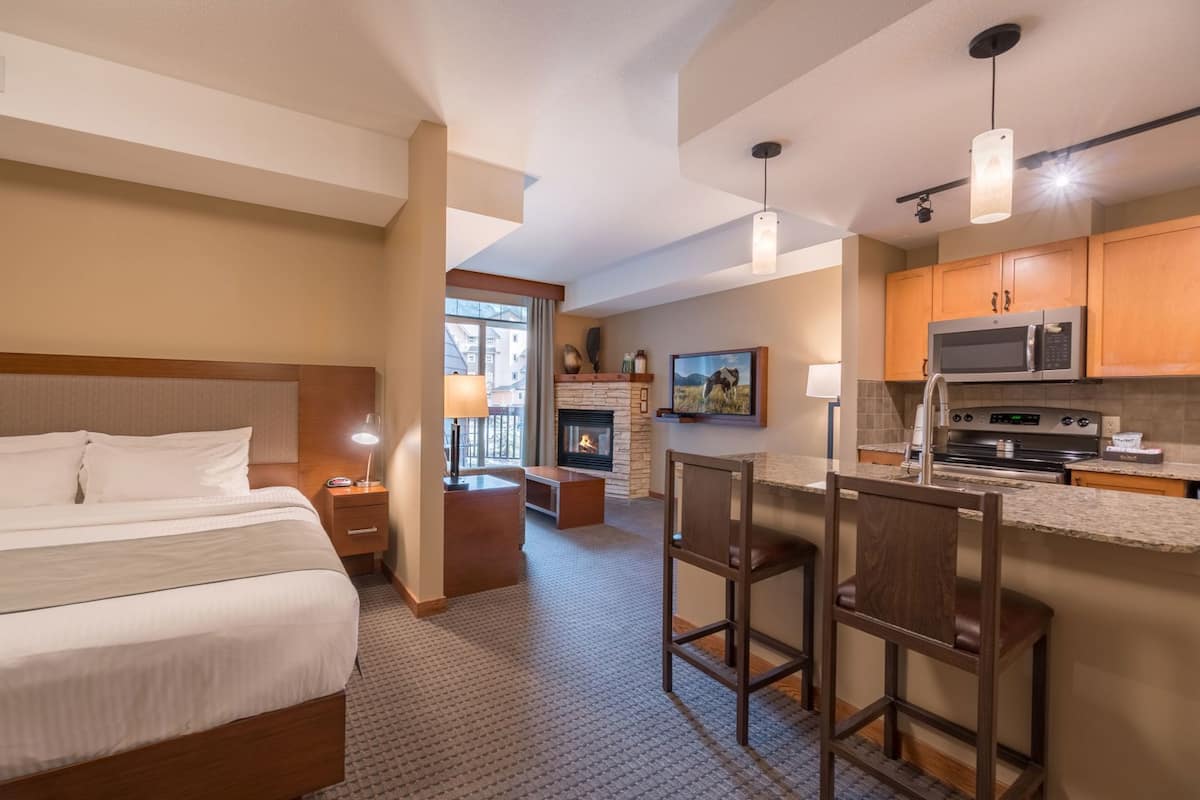 Habitación de hotel con cama, pequeña cocina con microondas y estufa, chimenea y televisor.