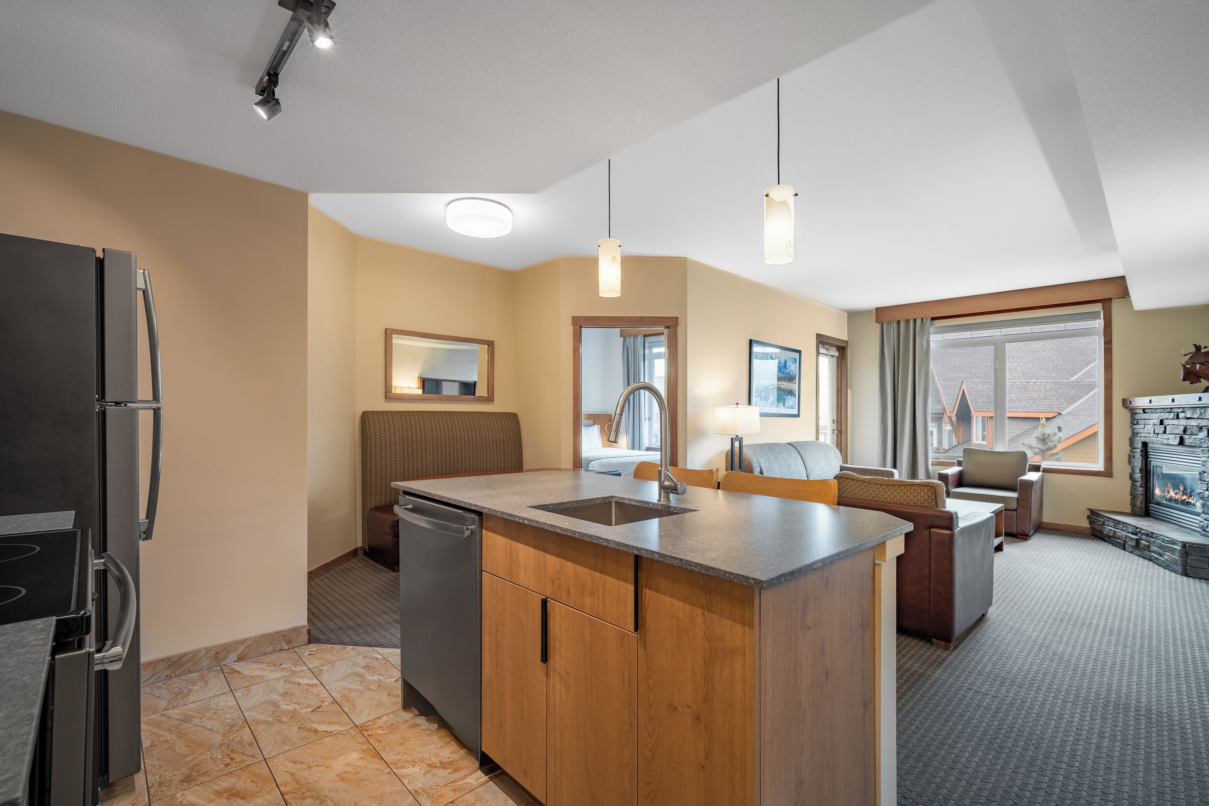A modern kitchen with a built-in island, a dishwasher, and a refrigerator. There is a seating area with a sofa and chairs, and a fireplace.