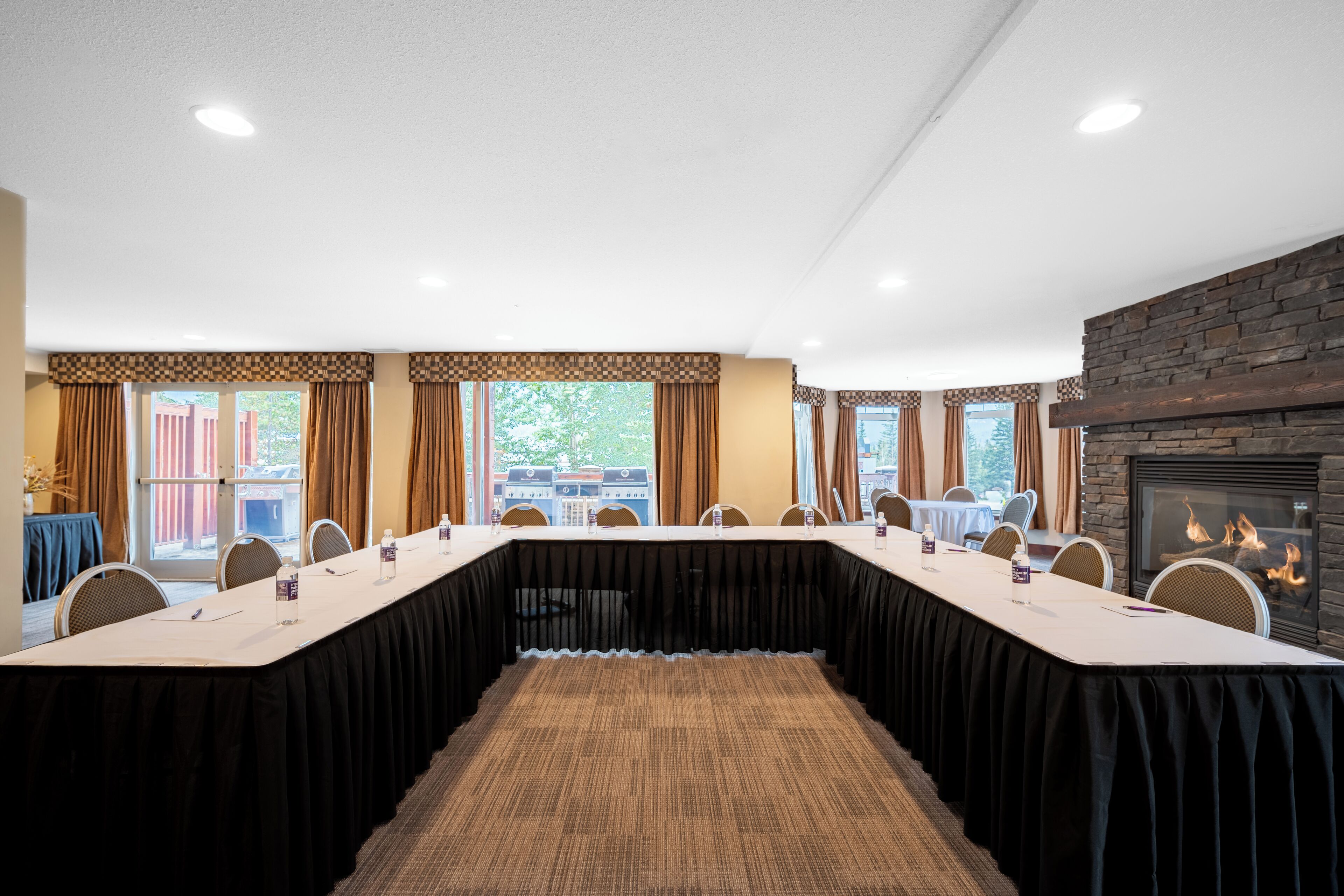Une salle de conférence avec une longue table, des chaises, une cheminée et des fenêtres avec des rideaux.