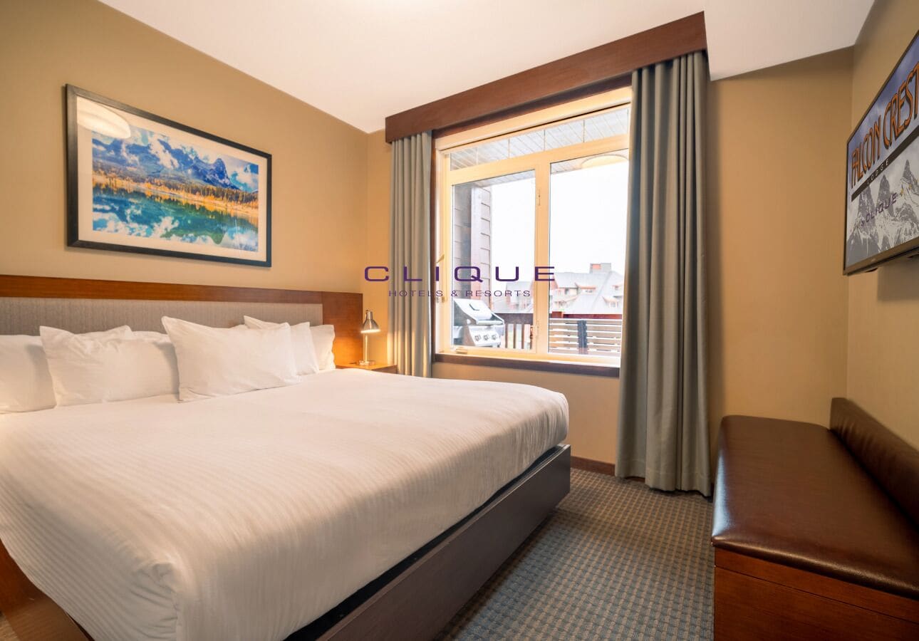 A hotel room with a large bed, a desk, a chair, a window with curtains, and a framed picture on the wall.