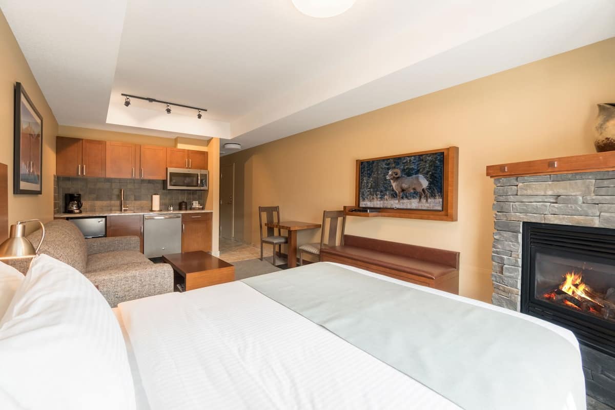 Una habitación de hotel con cama, chimenea, zona de comedor y kitchenette.