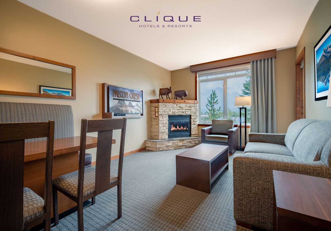 A hotel room with a fireplace, a sofa, a coffee table, and a dining area with chairs.