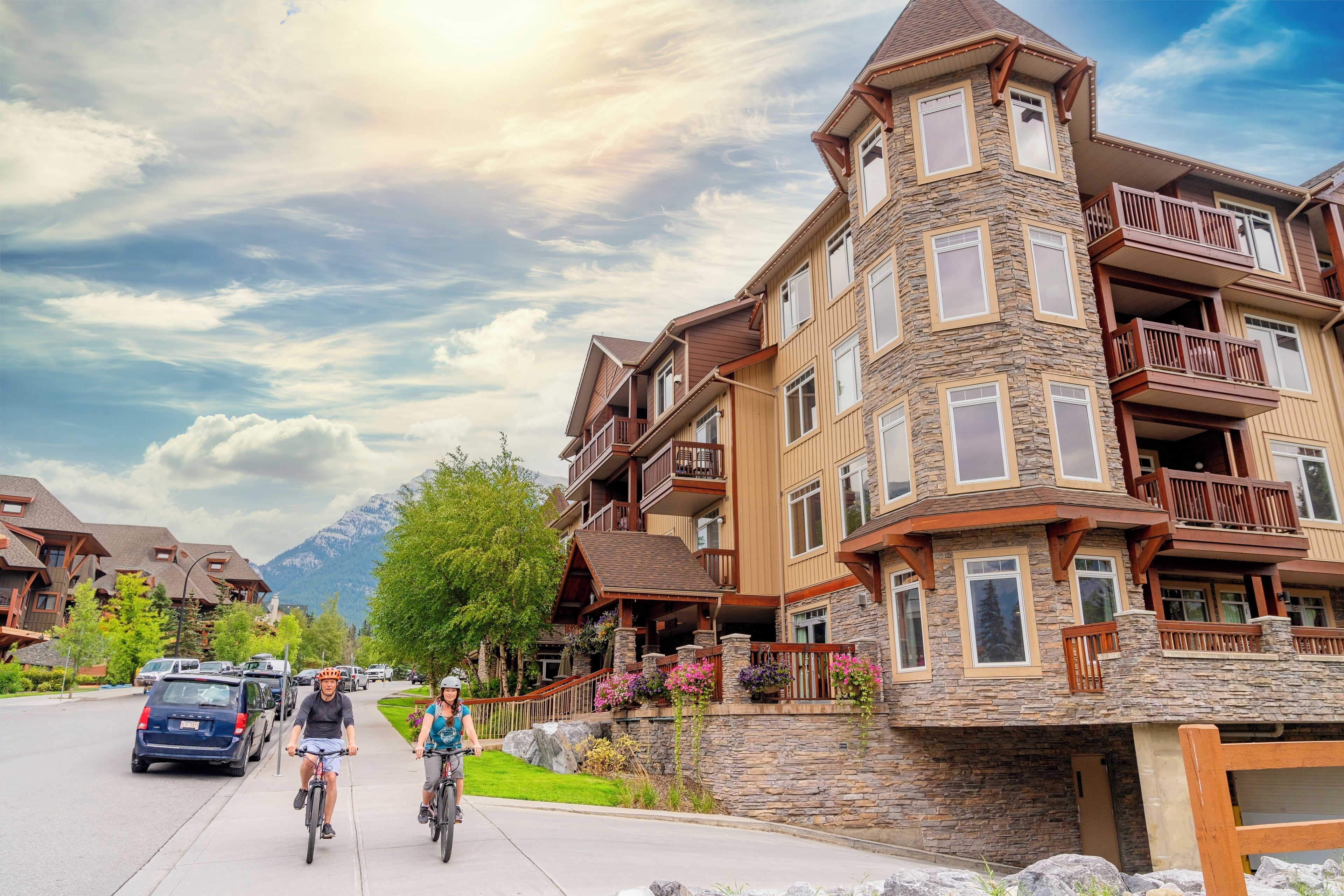 A multi-story building with stone and wood exterior, balconies, and a mountain backdrop.