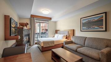 A hotel room with a bed, a sofa, a desk, a fireplace, and a balcony with a view of a mountain.