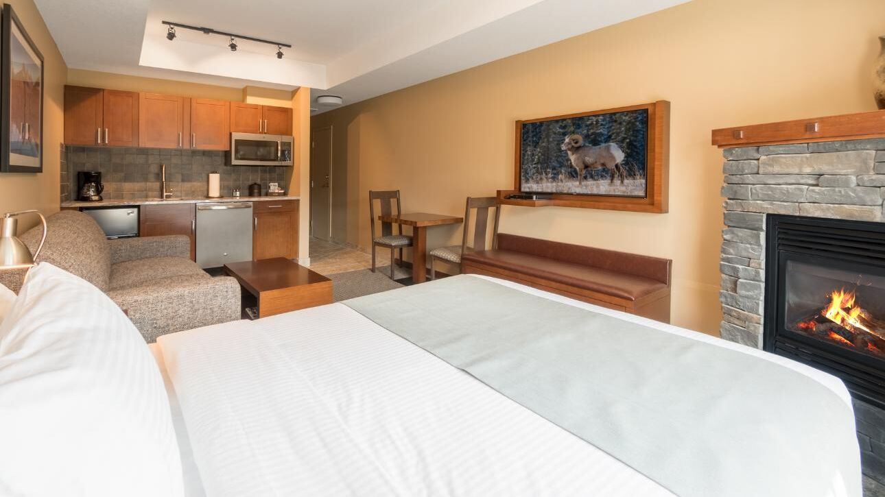 Habitación de hotel con cama, zona de estar con chimenea, kitchenette pequeña y un cuadro en la pared.