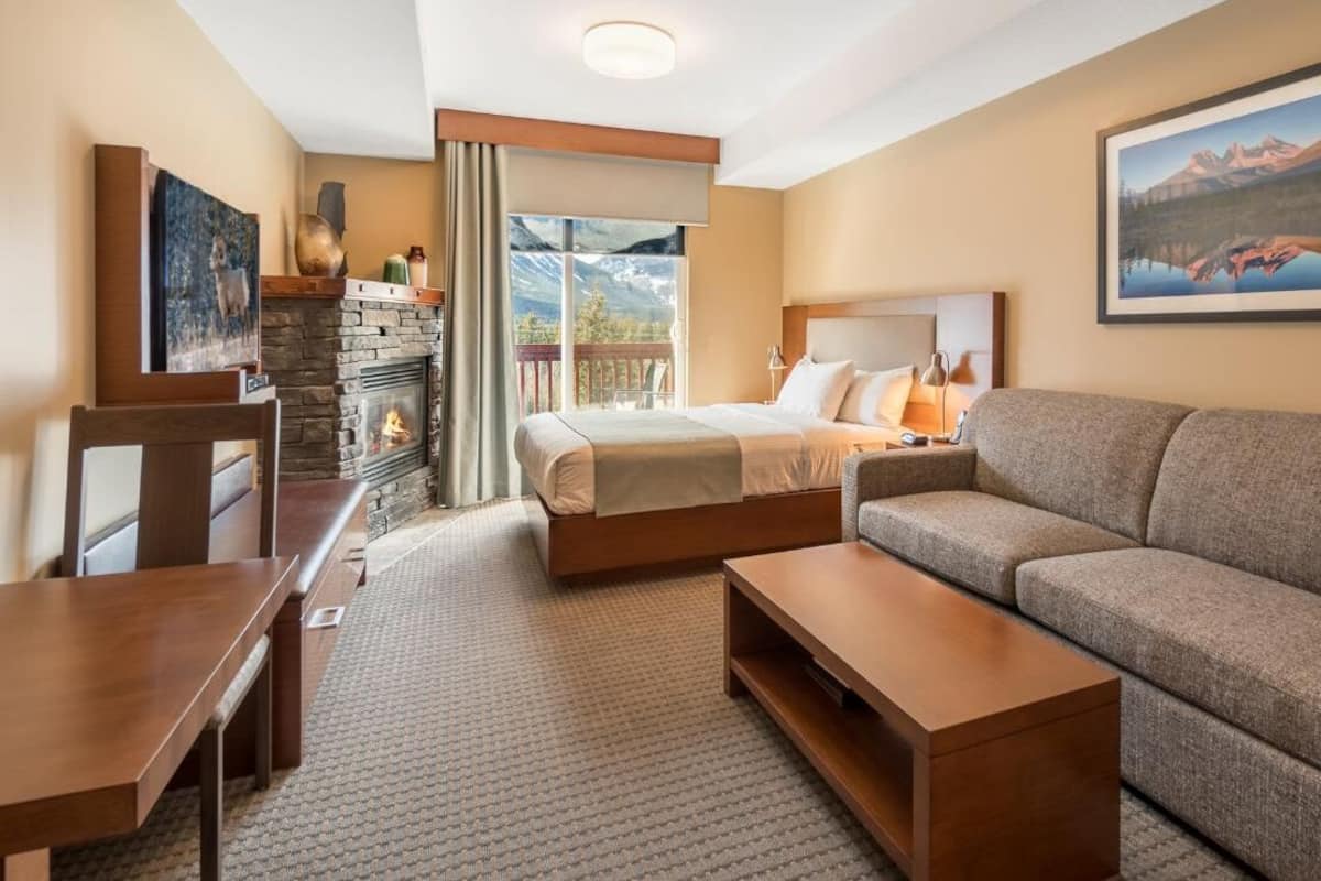 Habitación de hotel con cama, sofá, mesa de madera y chimenea.