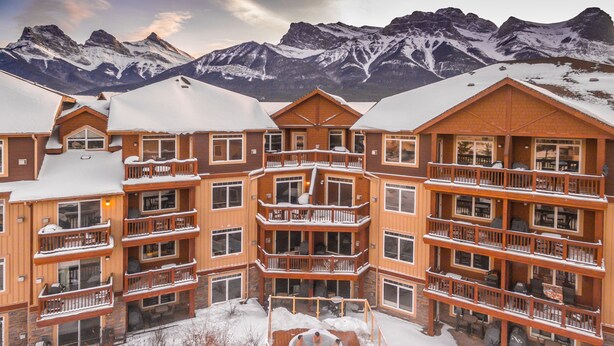 A multi-story hotel with balconies, a pool, and a snowy mountain backdrop. - Falcon Crest Lodge by CLIQUE (Canmore)