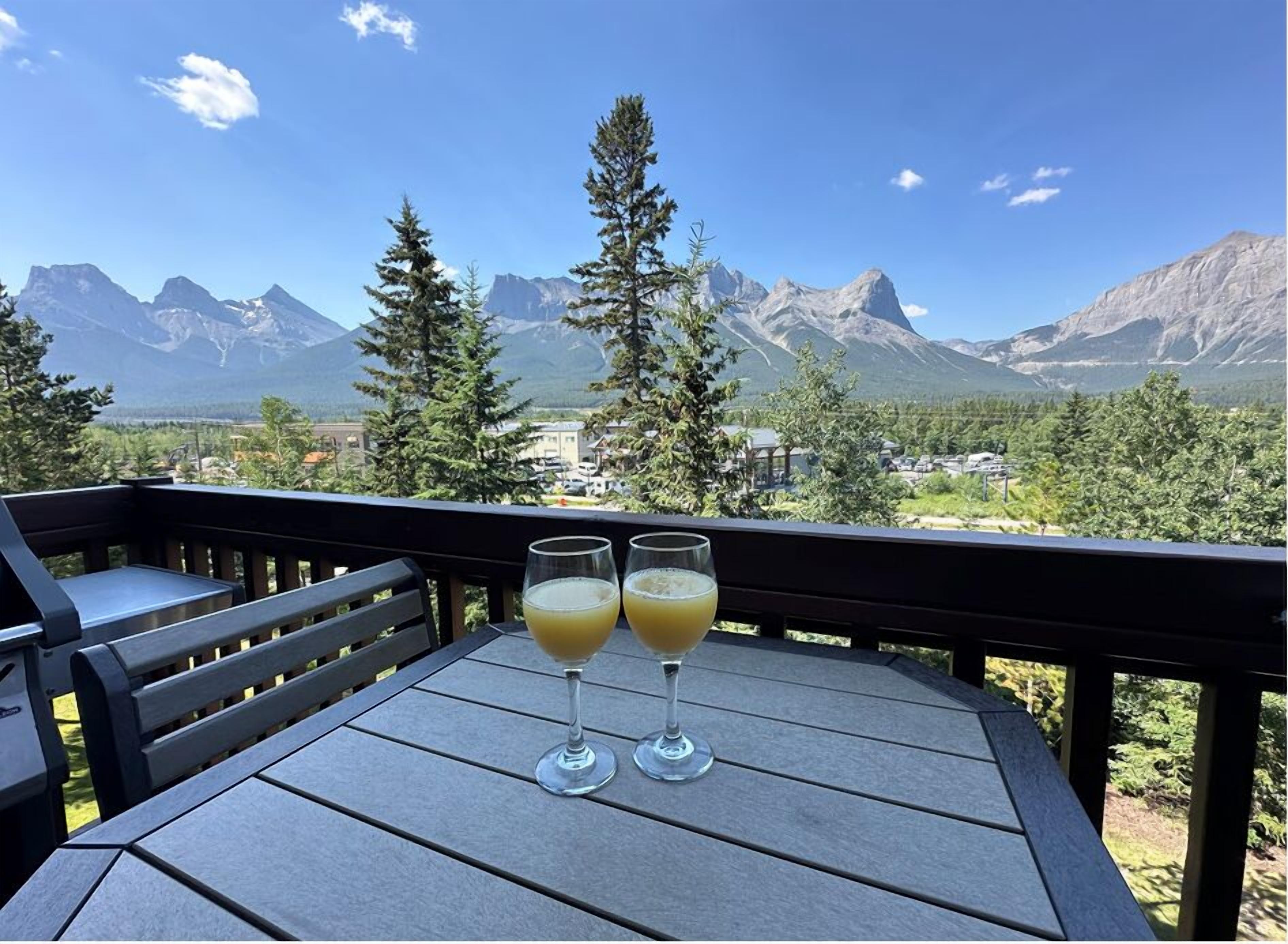 A balcony with two glasses of orange juice and a view of mountains.