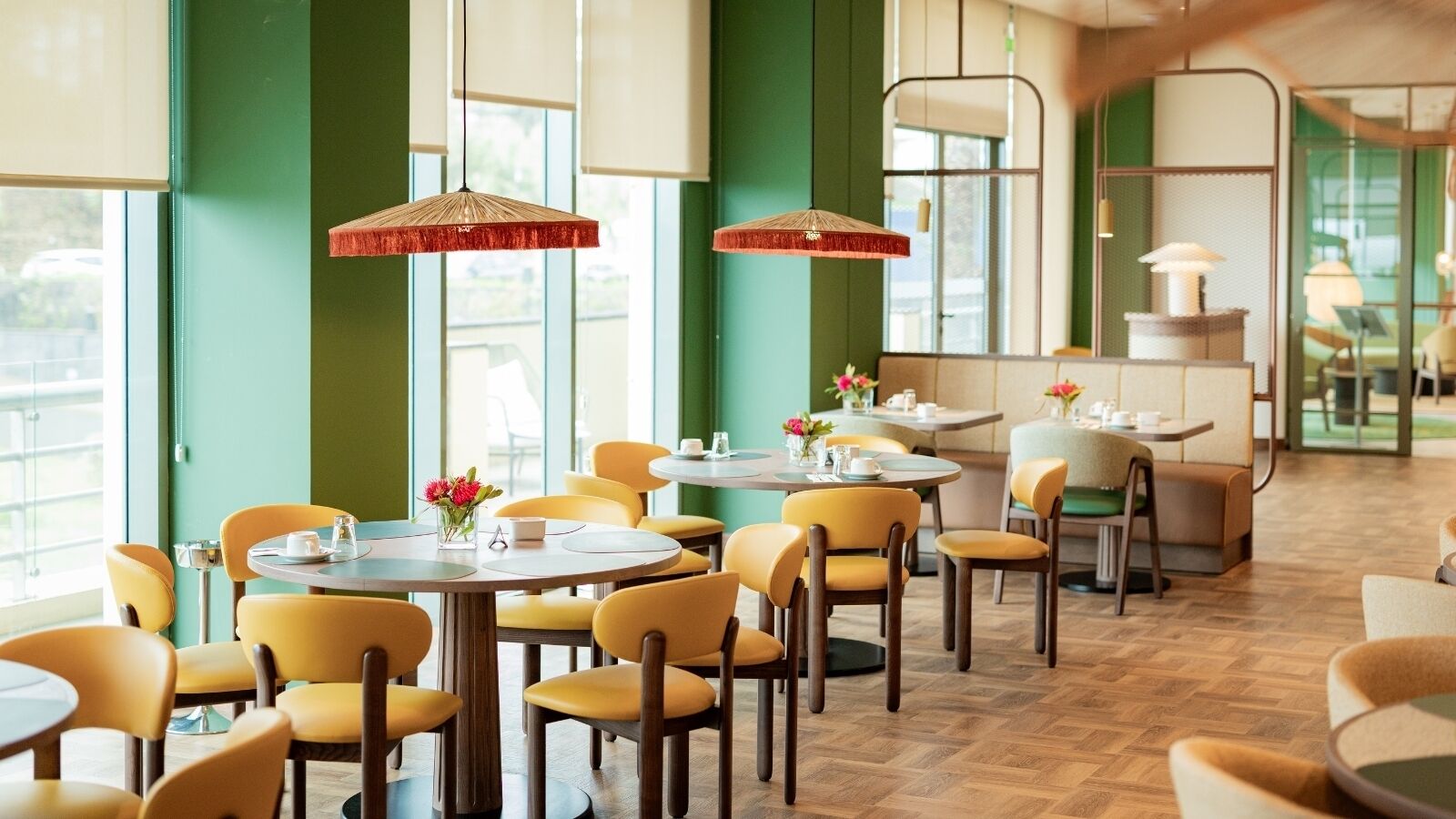 A restaurant with round tables, yellow chairs, and hanging red umbrellas.