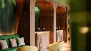 Zona de recepción con un sofá verde, dos sillones amarillos y un mostrador de madera con computadoras portátiles.