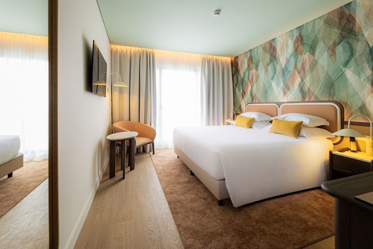 Una habitación de hotel con cama, mesitas de noche, una silla, escritorio y televisor.