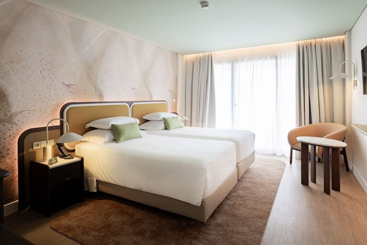Habitación de hotel con cama, mesitas de noche, escritorio, silla y televisor montado en la pared.