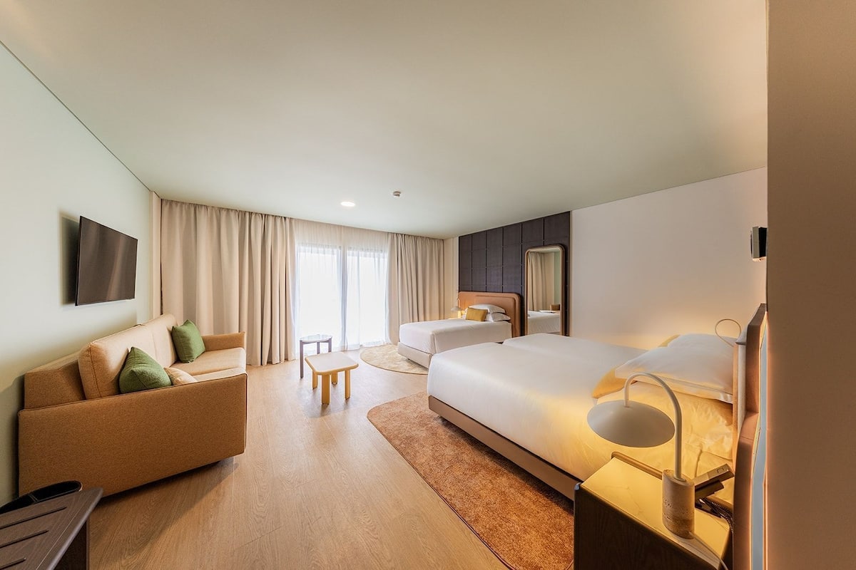 Una habitación de hotel con sofá, dos camas, televisor y espejo.