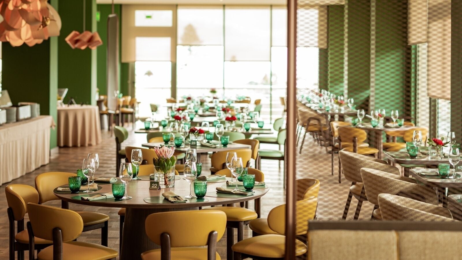 A restaurant with round tables, yellow chairs, and green glassware.