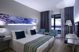 Habitación de hotel con una cama grande, dos sillas, un escritorio y un cuadro en la pared.