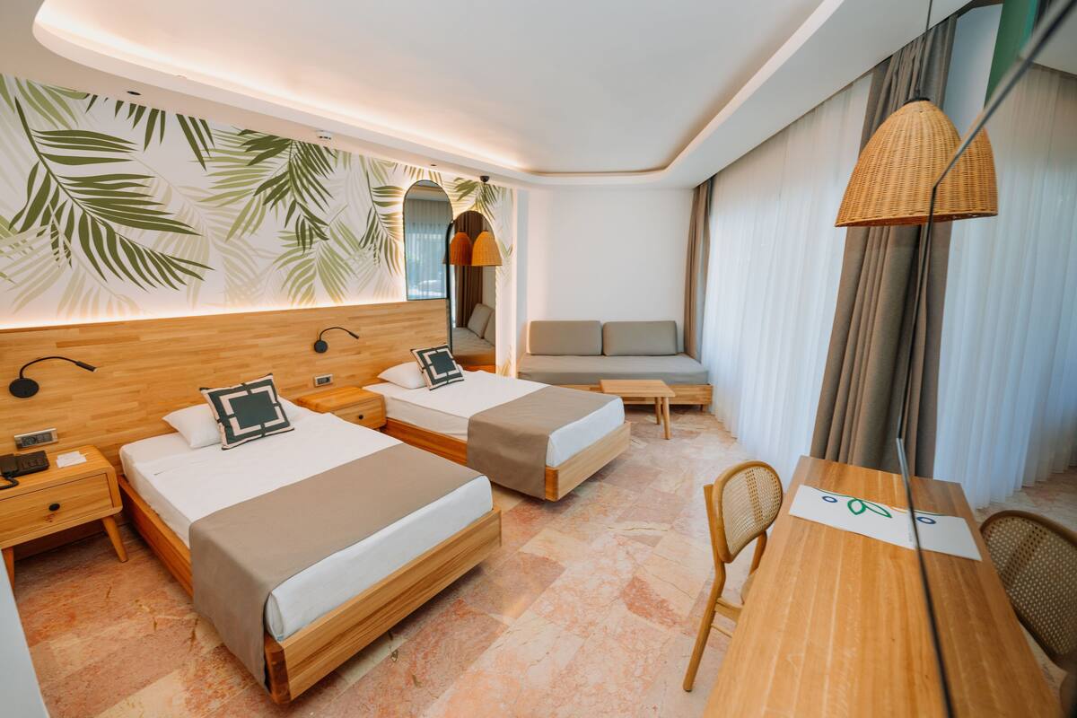 A modern hotel room with two beds, a sofa, a dining table, and a large window with curtains.