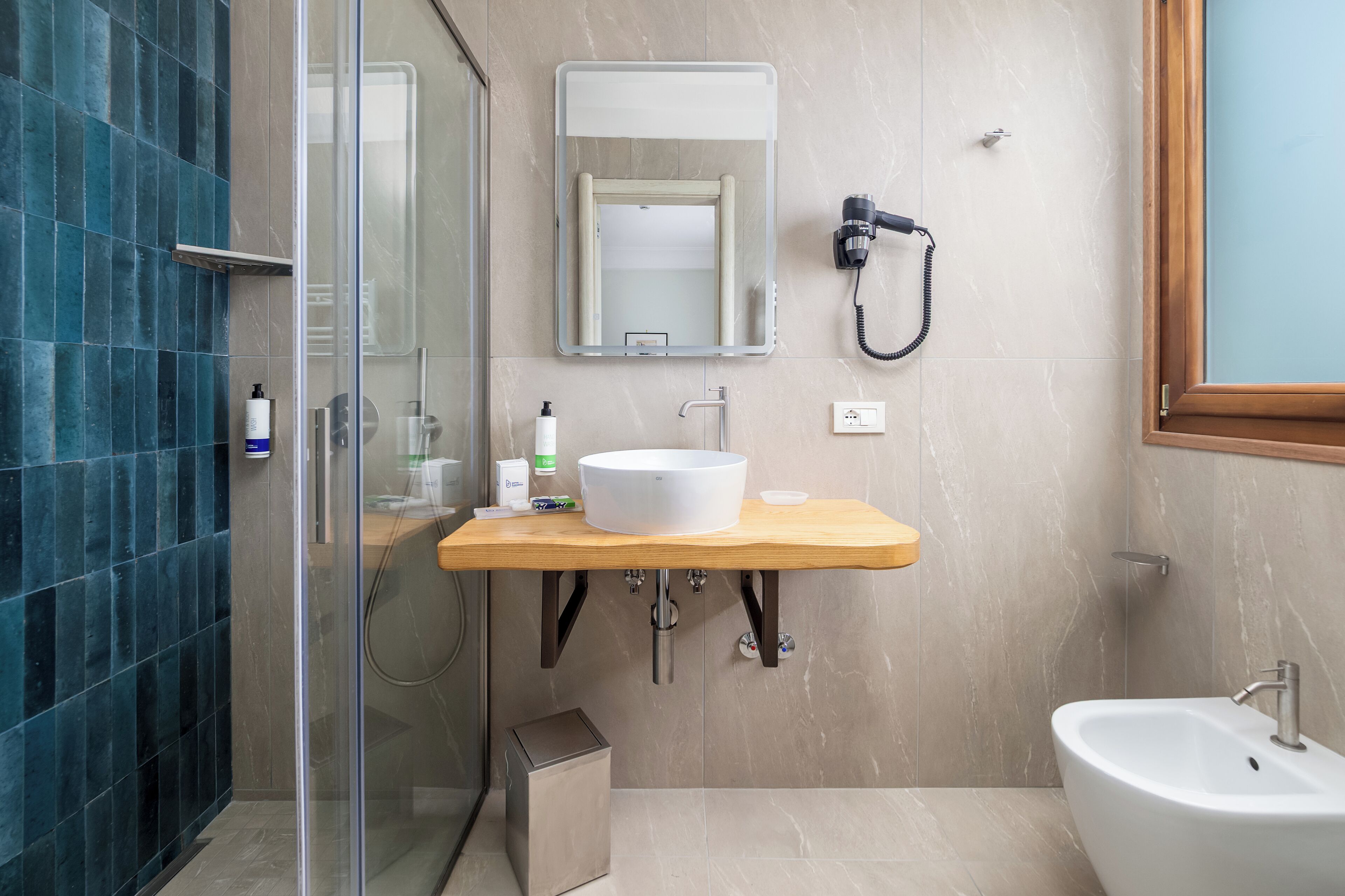 A modern bathroom with a glass shower enclosure, a wooden vanity with a white sink, and a bidet.