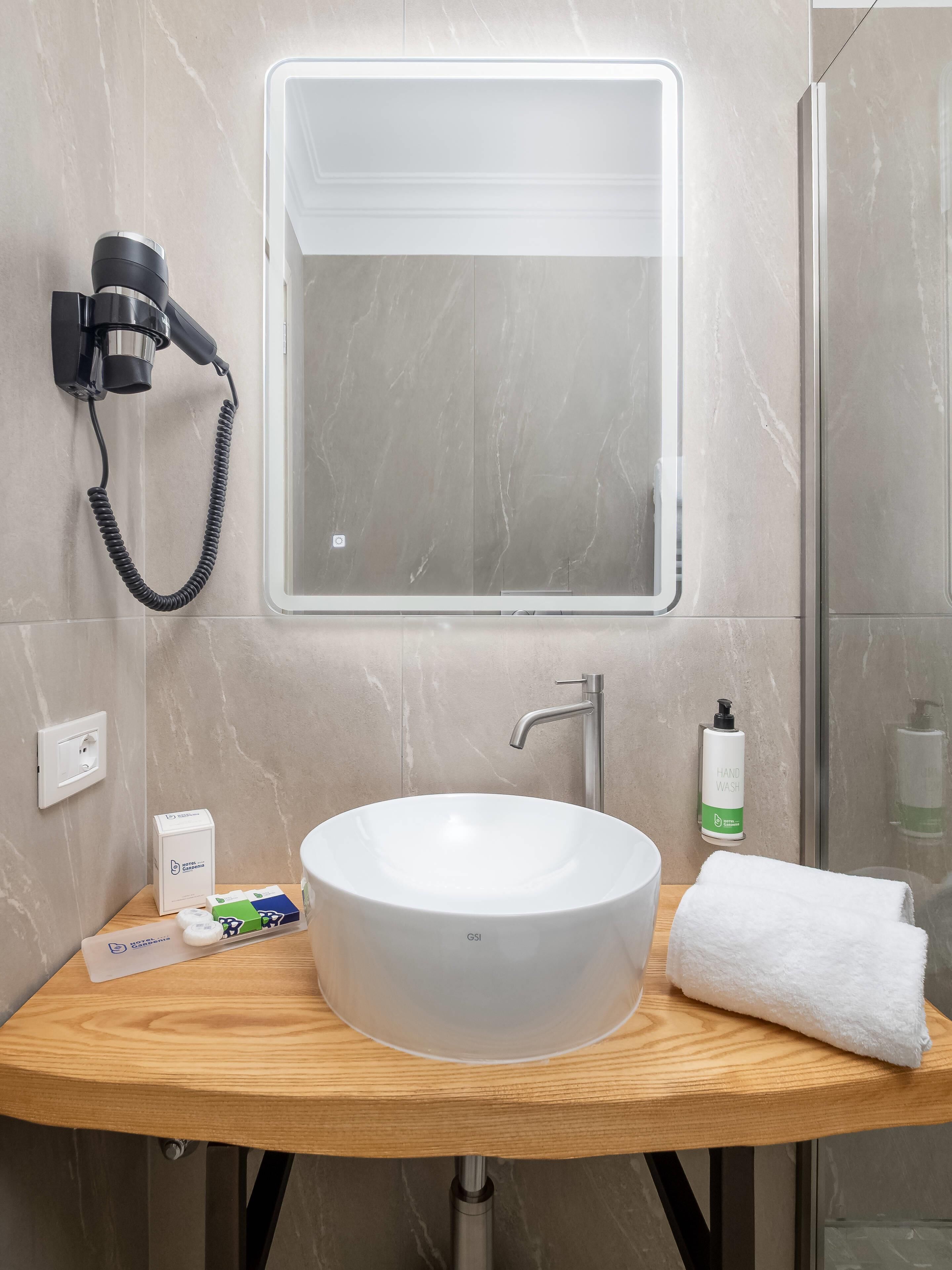 A bathroom with a round white sink, a handheld hair dryer, a hand wash bottle, and a towel on the counter.