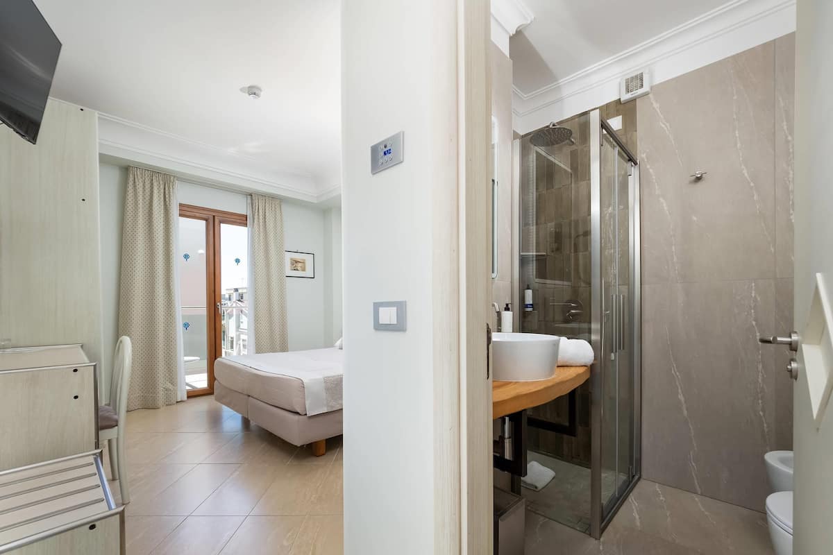 Une chambre d’hôtel avec un lit, une salle de bain avec douche et un balcon avec des rideaux.
