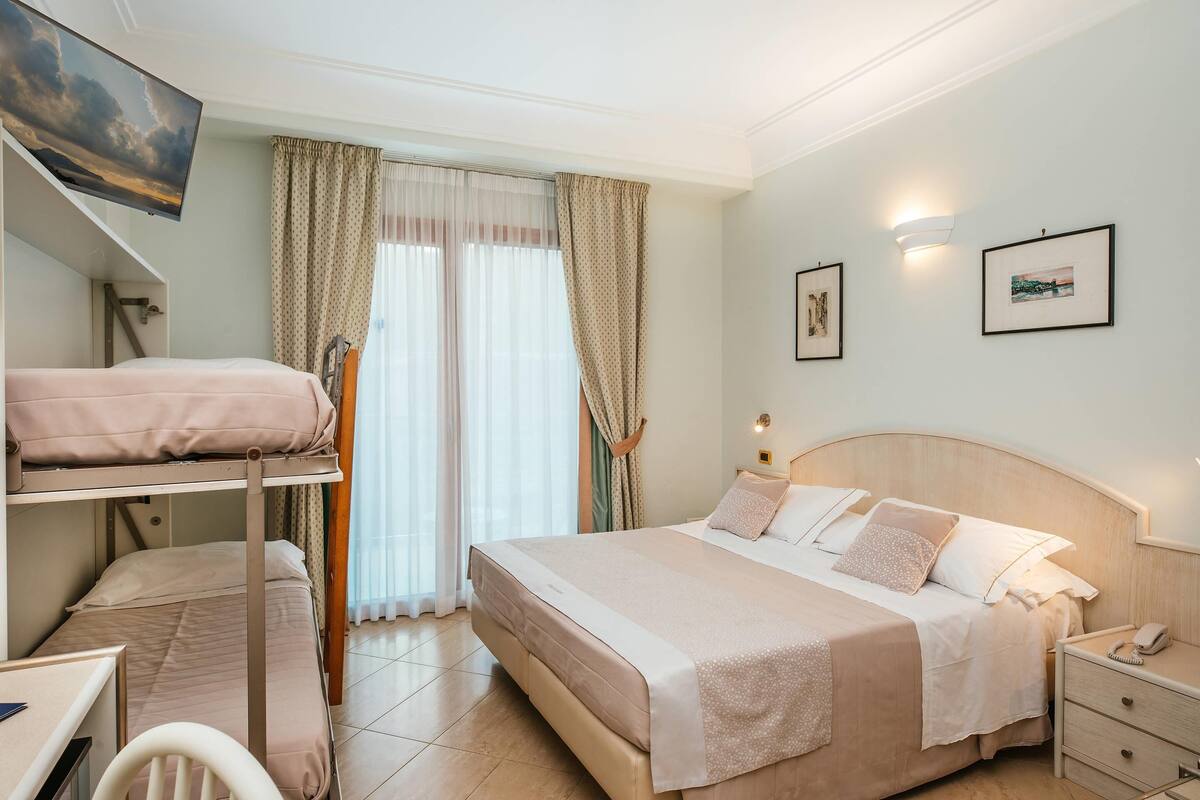 Une chambre d’hôtel avec des lits superposés, un bureau, une table de chevet avec une lampe et des œuvres d’art accrochées aux murs.