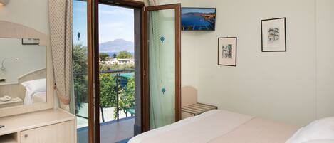 Habitación de hotel con cama, escritorio, silla y balcón con vista al mar y a las montañas.