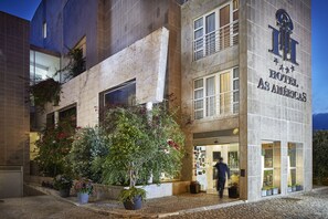 Exterior de hotel con fachada de piedra, ventanas amplias y plantas en macetas.
