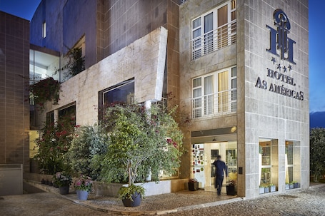 Exterior de hotel con fachada de piedra, ventanas amplias y plantas en macetas.