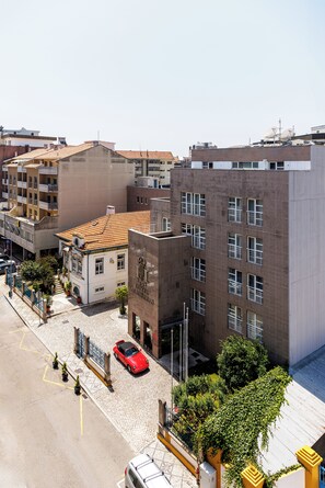 A hotel with a tiled roof, a courtyard with potted plants, and a red car parked in front.