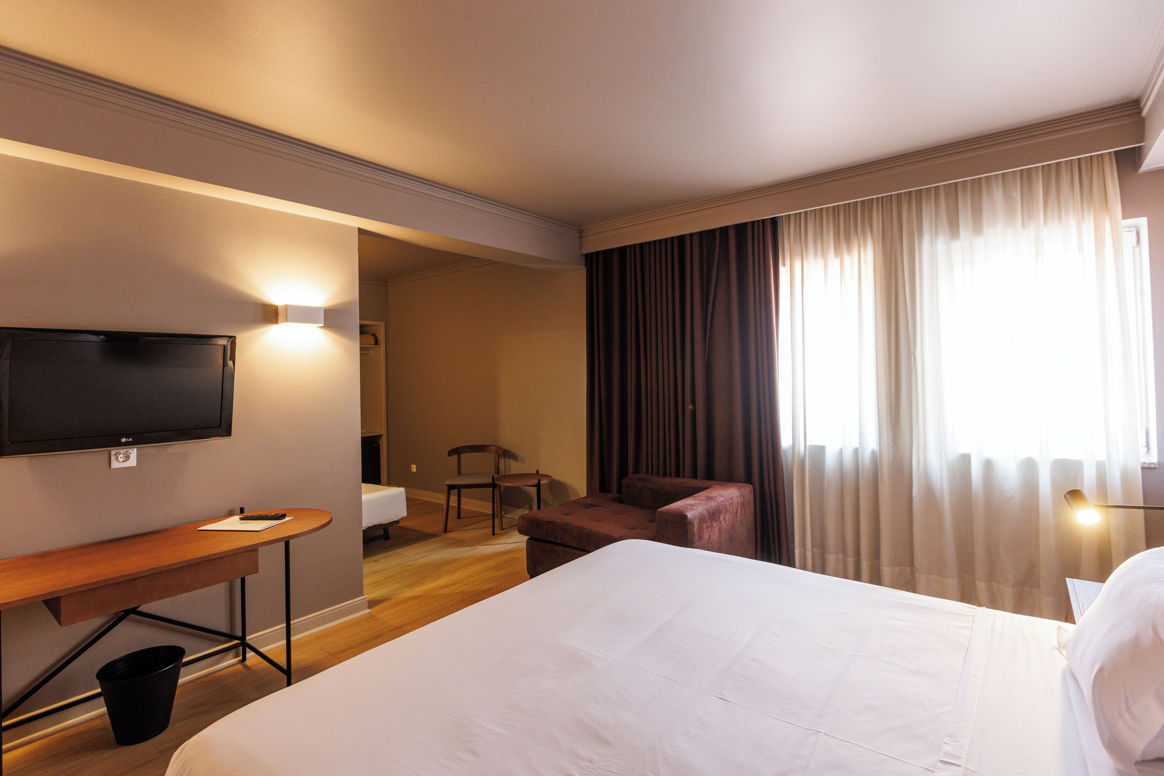 A hotel room with a bed, a desk, a chair, a television, and a window with curtains.