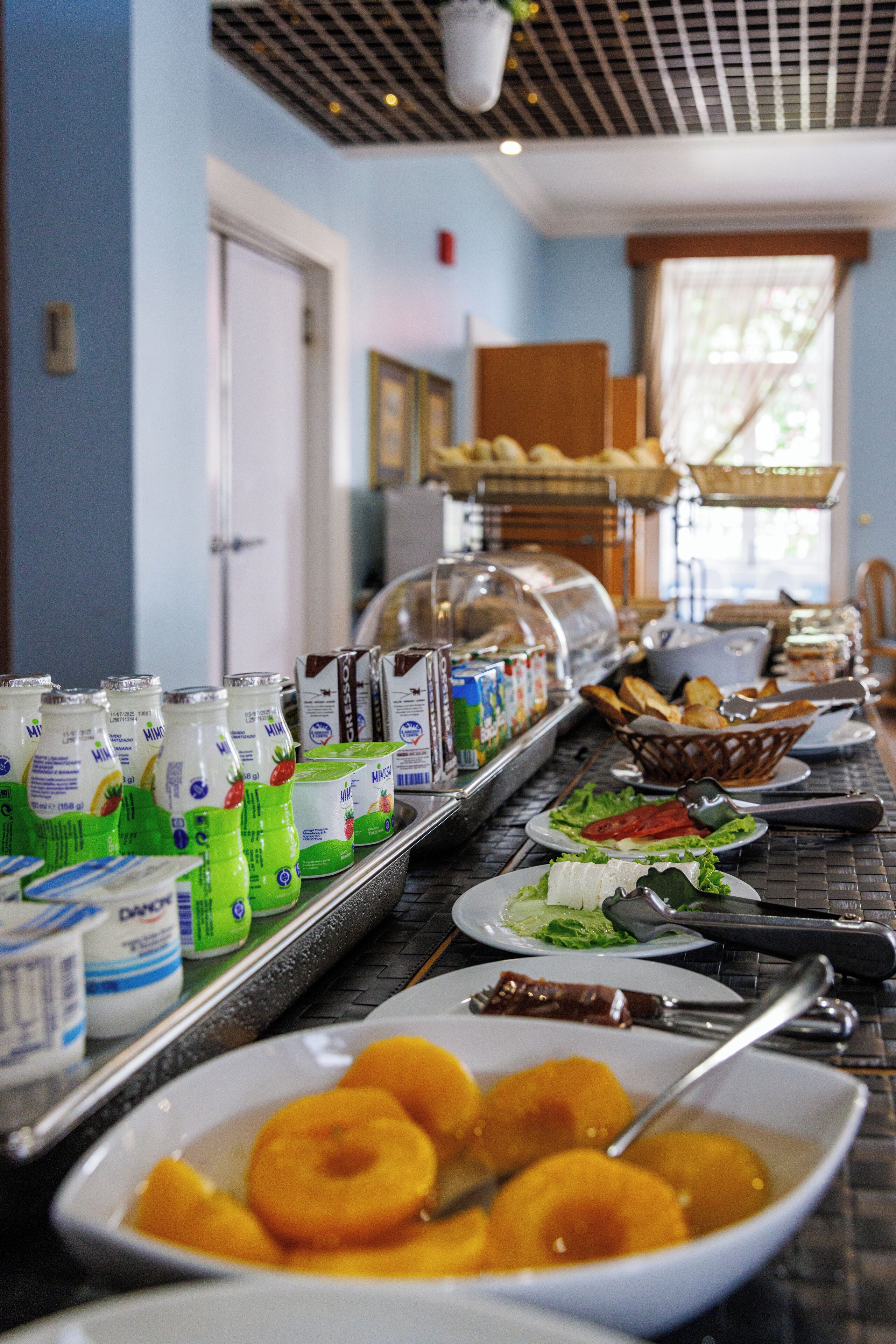 A buffet with various food items and beverages, including yogurt, bread, and fruits.