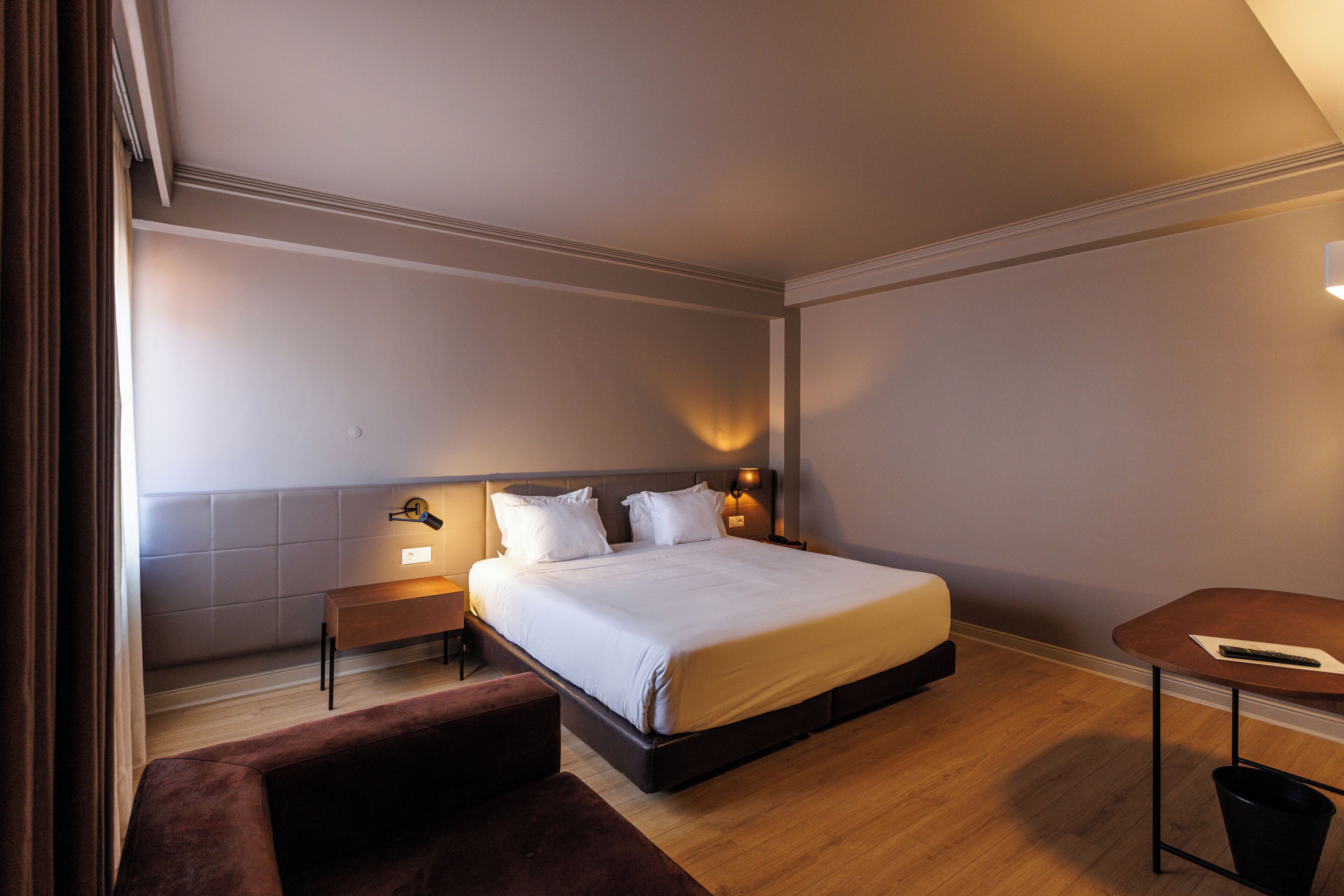 Una habitación de hotel con una cama grande, mesitas de noche, un escritorio pequeño y una silla.
