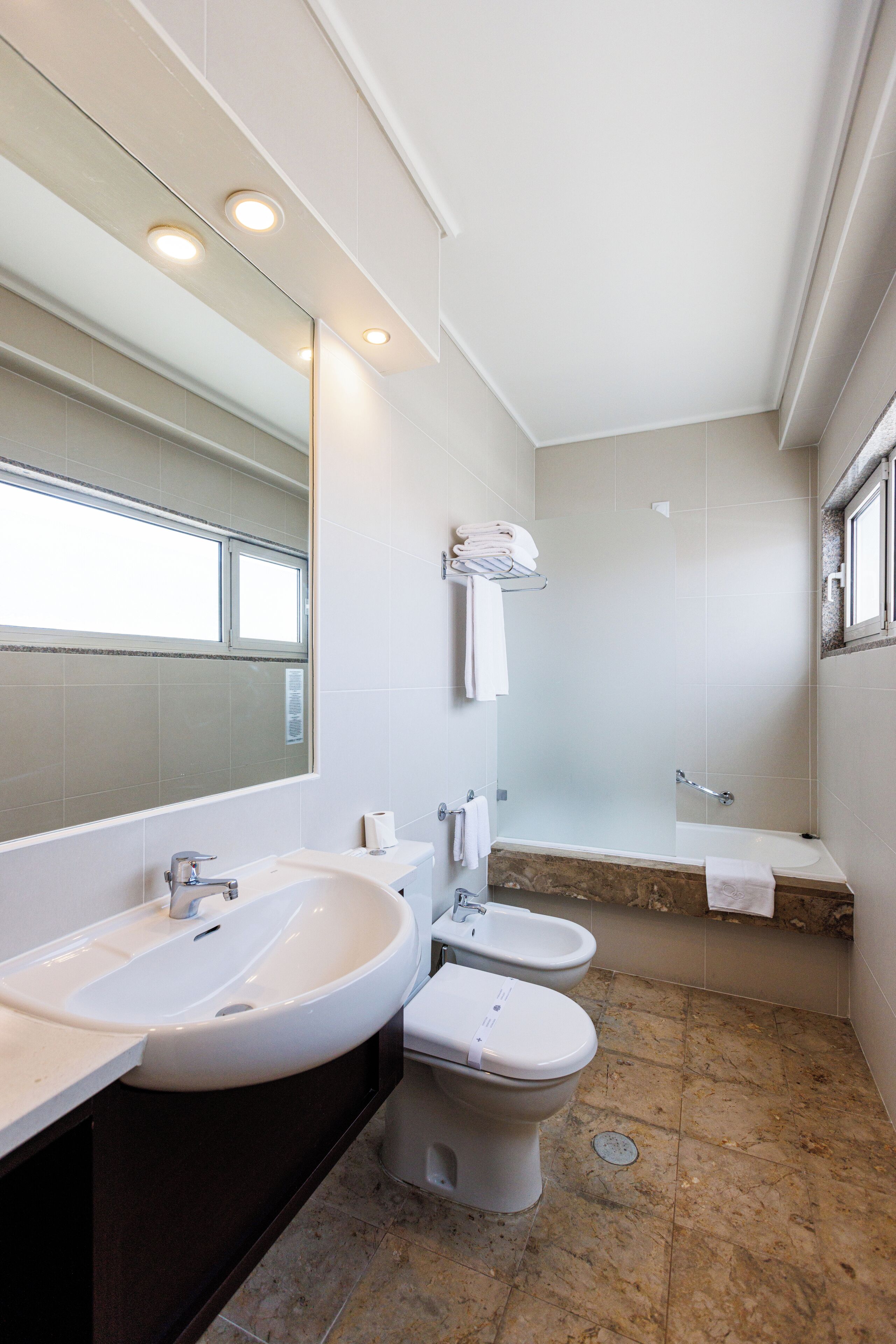 A modern bathroom with a large mirror, two sinks, a bidet, and a bathtub.