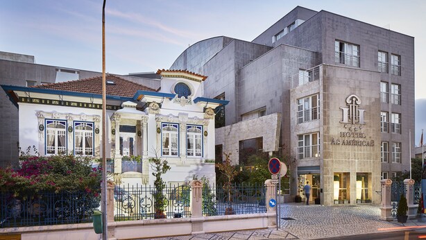 Un hotel con fachada clásica, un edificio moderno contiguo, y una calle empedrada.