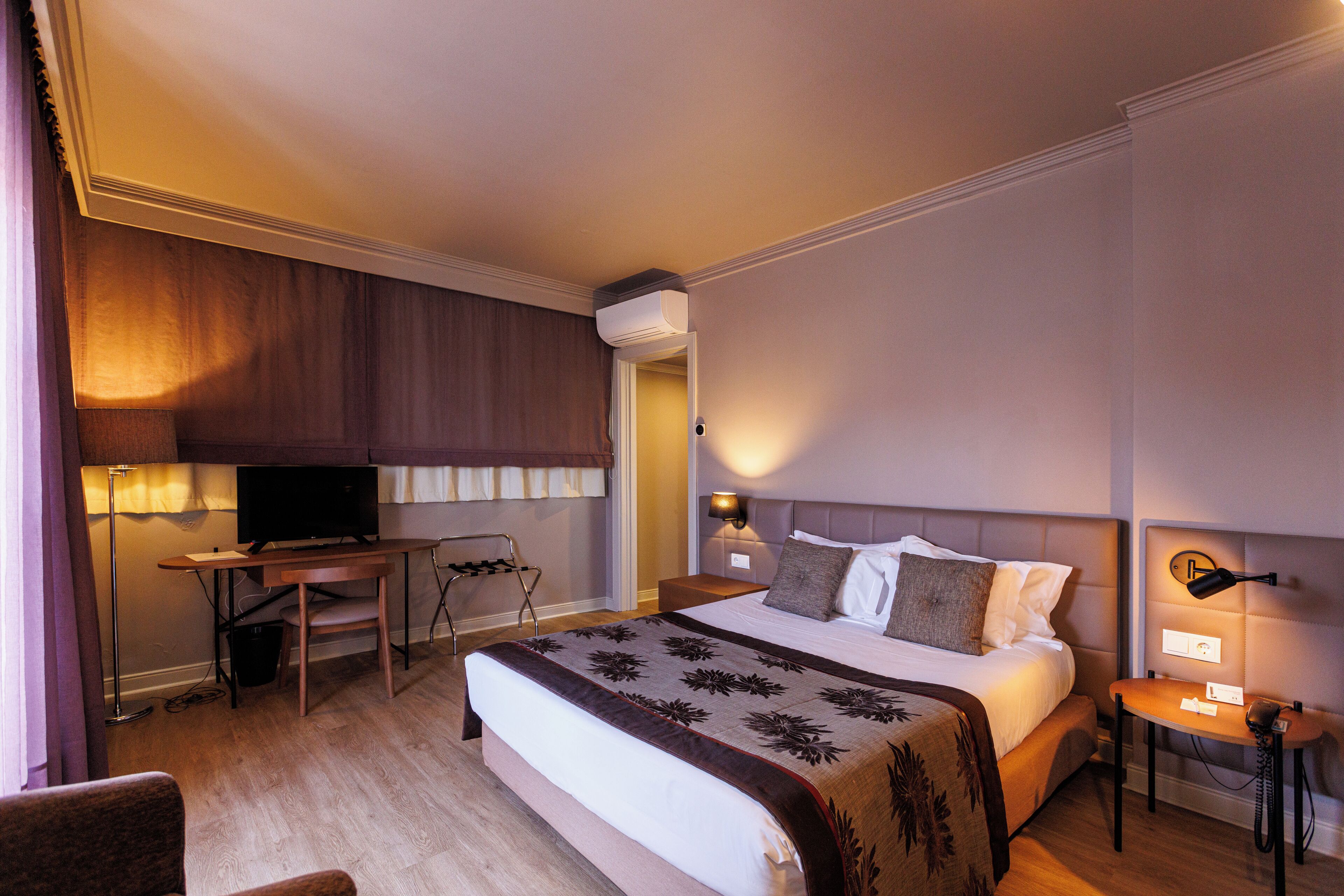 Una habitación de hotel con cama, escritorio, televisor, lámpara y teléfono.
