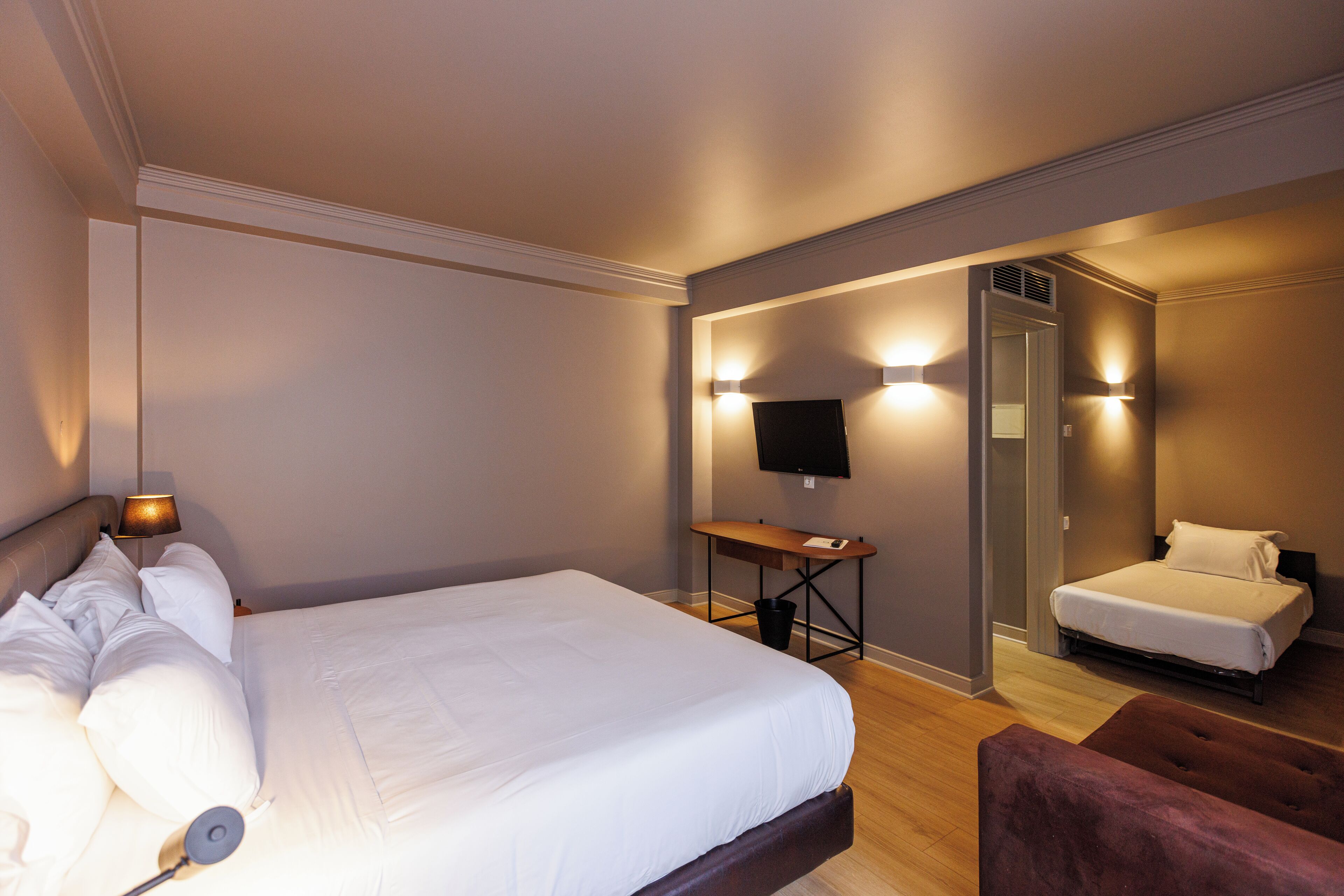 A hotel room with a large bed, a desk, a chair, and a TV mounted on the wall.