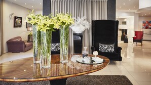 Una sala moderna con una mesa de centro de vidrio, jarrones con flores, un sofá y un sillón negro.