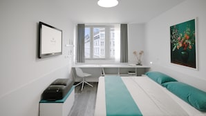 A modern hotel room with a bed, desk, chair, and a window with a city view. - AllYouNeed Hotel Vienna 2 (Vienna)