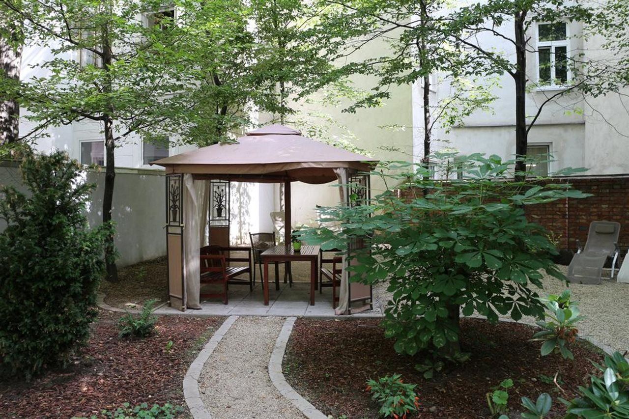 A gazebo with a table and chairs, surrounded by trees and a brick wall.