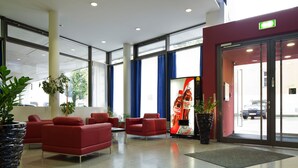 A modern lobby with red seating, large windows, and a Coca-Cola advertisement. - Allyouneed Hotel Salzburg (Salzburg)