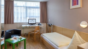A hotel room with a bed, a desk with a computer, a chair, and a small table with a cup and a book. - Allyouneed Hotel Salzburg (Salzburg)