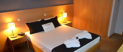 A neatly made bed with white linens, two bedside lamps, a telephone, and a folded towel on the bed.